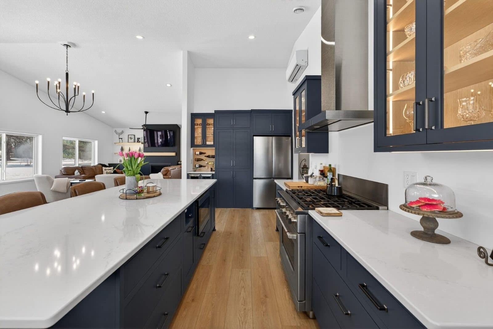 Kitchen with navy cabinets, a quartz island, a stainless hood and lit glass upper cabinets