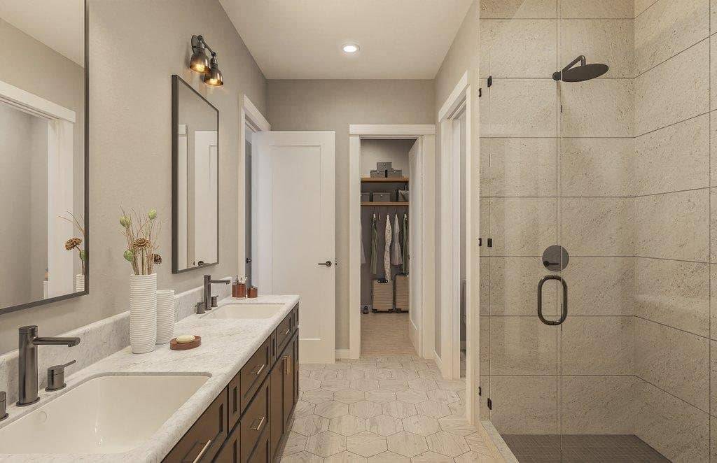 Primary bath with a double vanity, stone countertop and a frameless glass shower