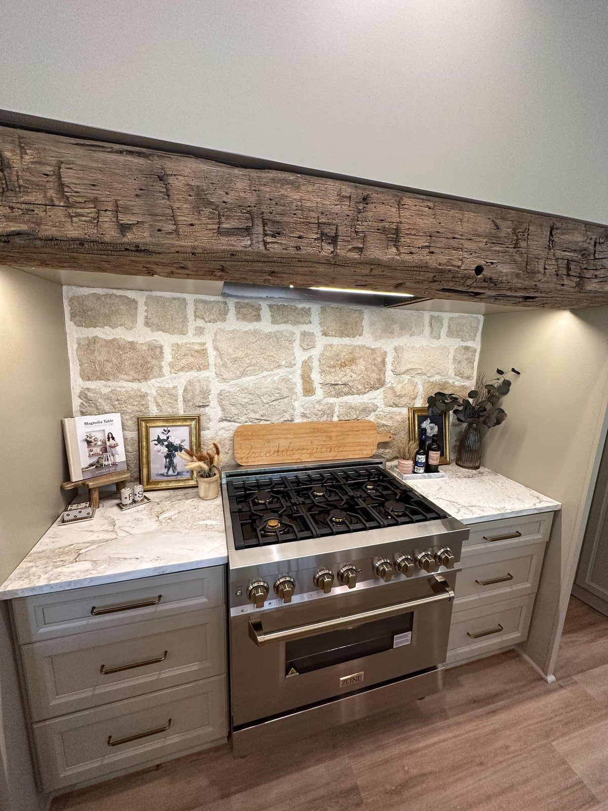 Range wall with a marble countertop, limestone backsplash and a reclaimed timber beam above