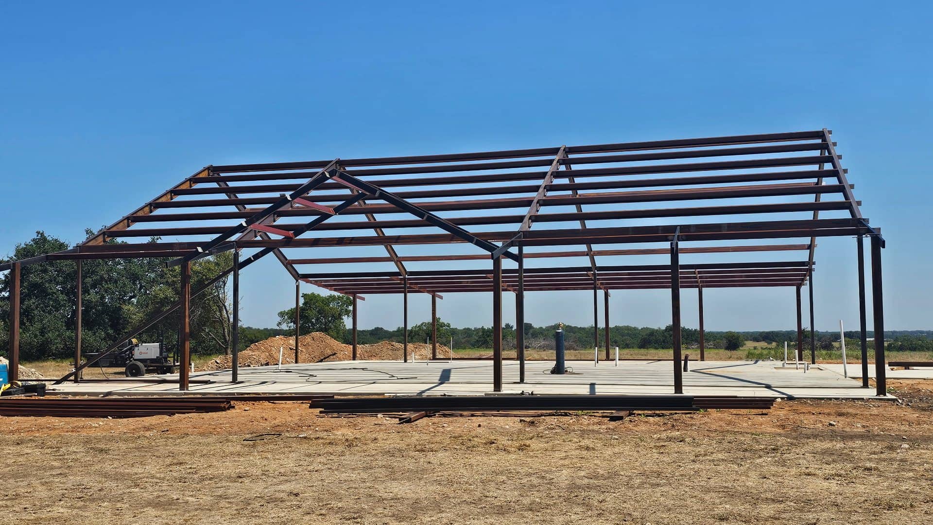 red iron frame clear span erected over slab rural site blue sky